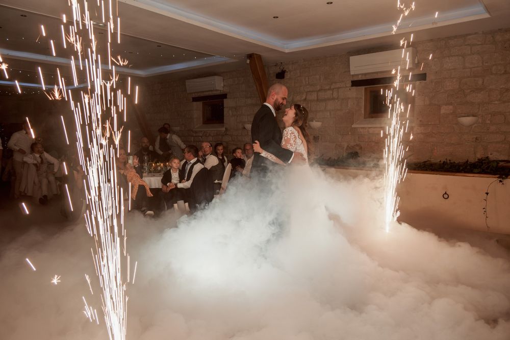 Newlyweds' first dance in a cloud of heavy fog between two cold spark fountains