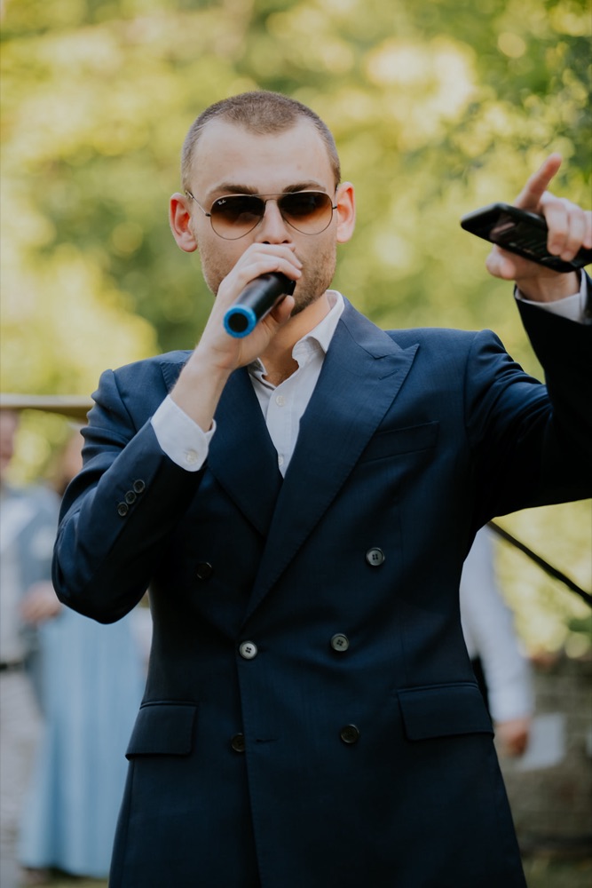 Bastien Marie, DJ de mariage, au micro en costume bleu marine pendant un vin d'honneur